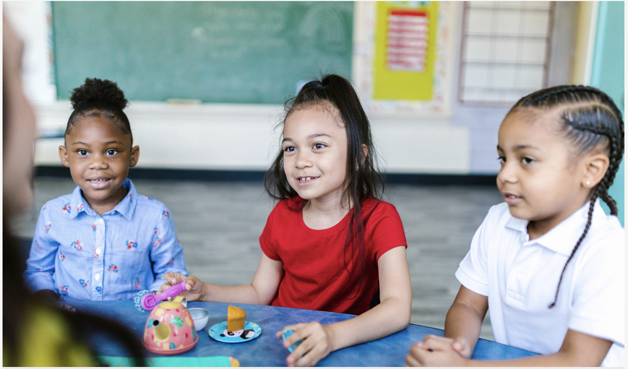three young children smiling in a classroom around a table
